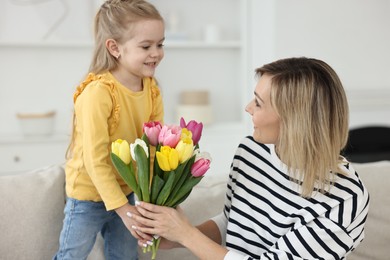 Little daughter congratulating her mom with bouquet of beautiful tulips at home. Happy Mother's Day