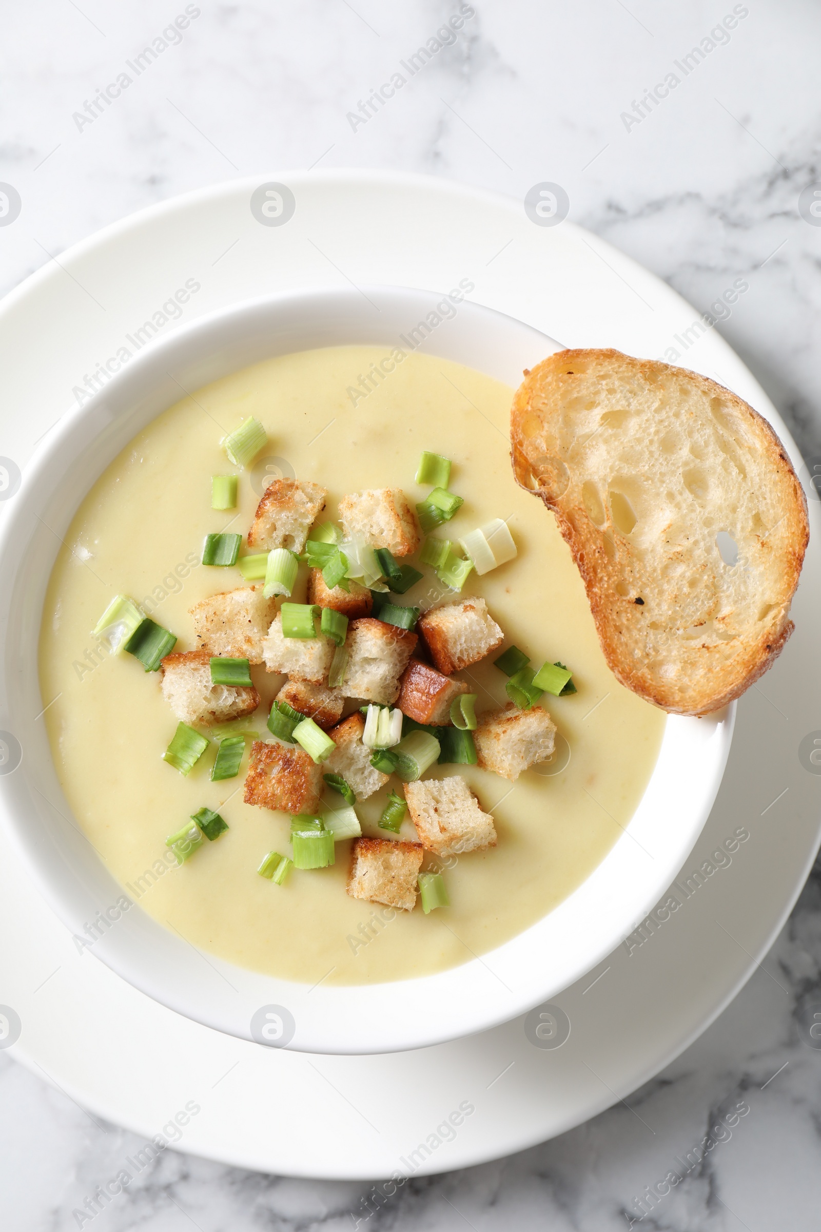 Photo of Tasty potato soup with croutons and green onion in bowl on white marble table, top view