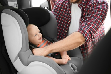 Photo of Father fastening baby to child safety seat inside of car