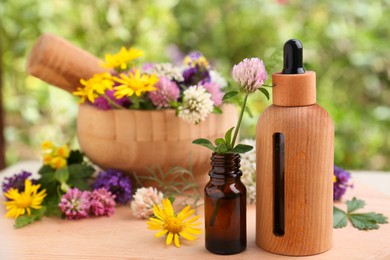 Bottles of essential oil and flowers on wooden table, closeup