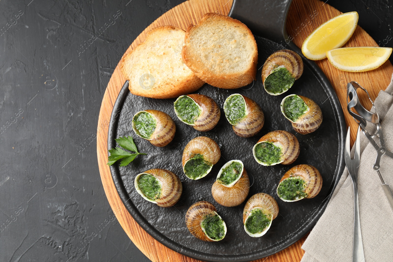 Photo of Delicious cooked snails served on grey textured table, flat lay