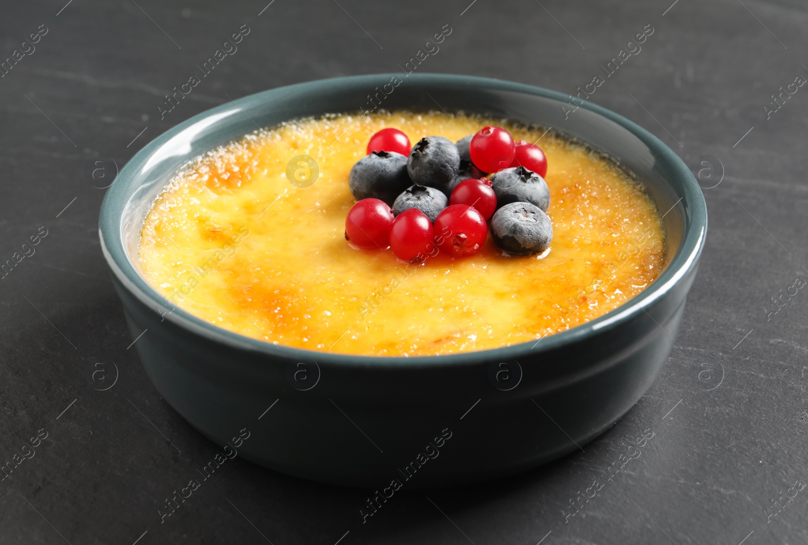 Photo of Delicious creme brulee with fresh berries on black table, closeup view