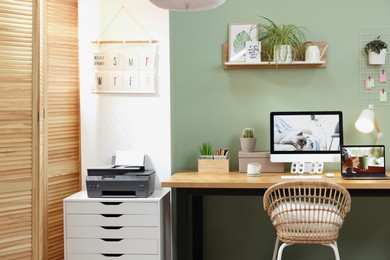 Stylish workplace with computer, laptop and lamp near olive wall at home