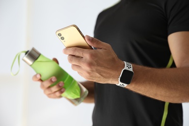 Photo of Man with smartphone and fitness tracker indoors, closeup