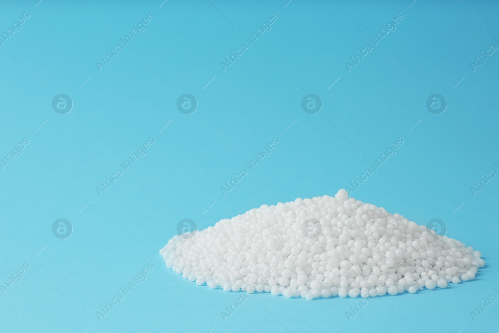 Photo of Pellets of ammonium nitrate on light blue background, space for text. Mineral fertilizer