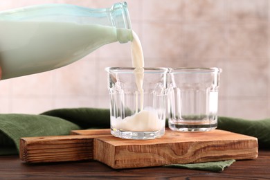 Pouring milk from bottle into glass at wooden table, closeup