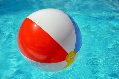 Colorful beach ball floating in swimming pool on sunny day. Space for text