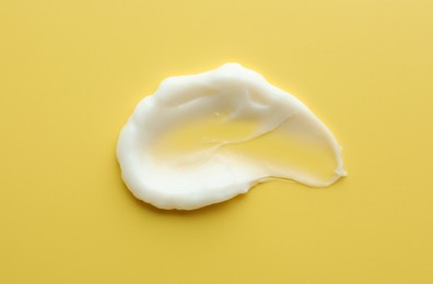 Photo of Sample of face cream on yellow background, top view