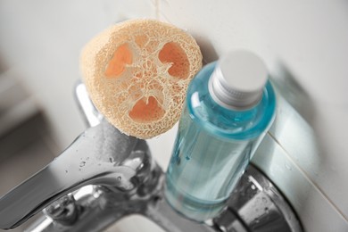 Photo of Natural loofah sponge and shower gel bottle on faucet in bathroom, above view