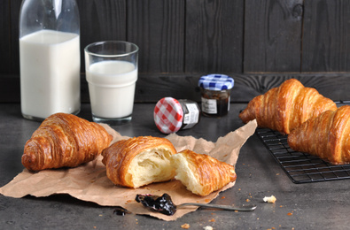 Photo of Tasty fresh croissants with jam and milk on grey table