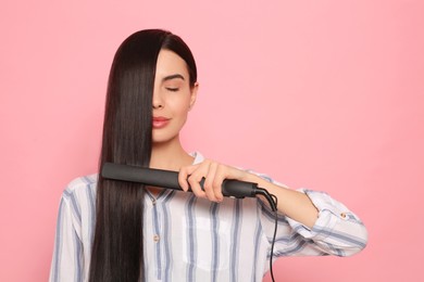 Photo of Beautiful woman using hair iron on pink background