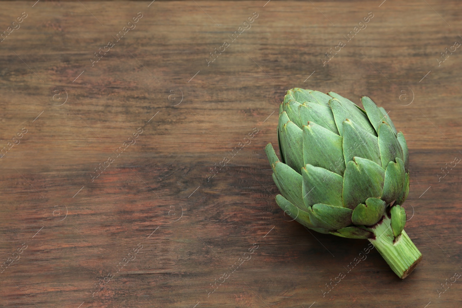 Photo of Fresh raw artichoke on wooden table. Space for text