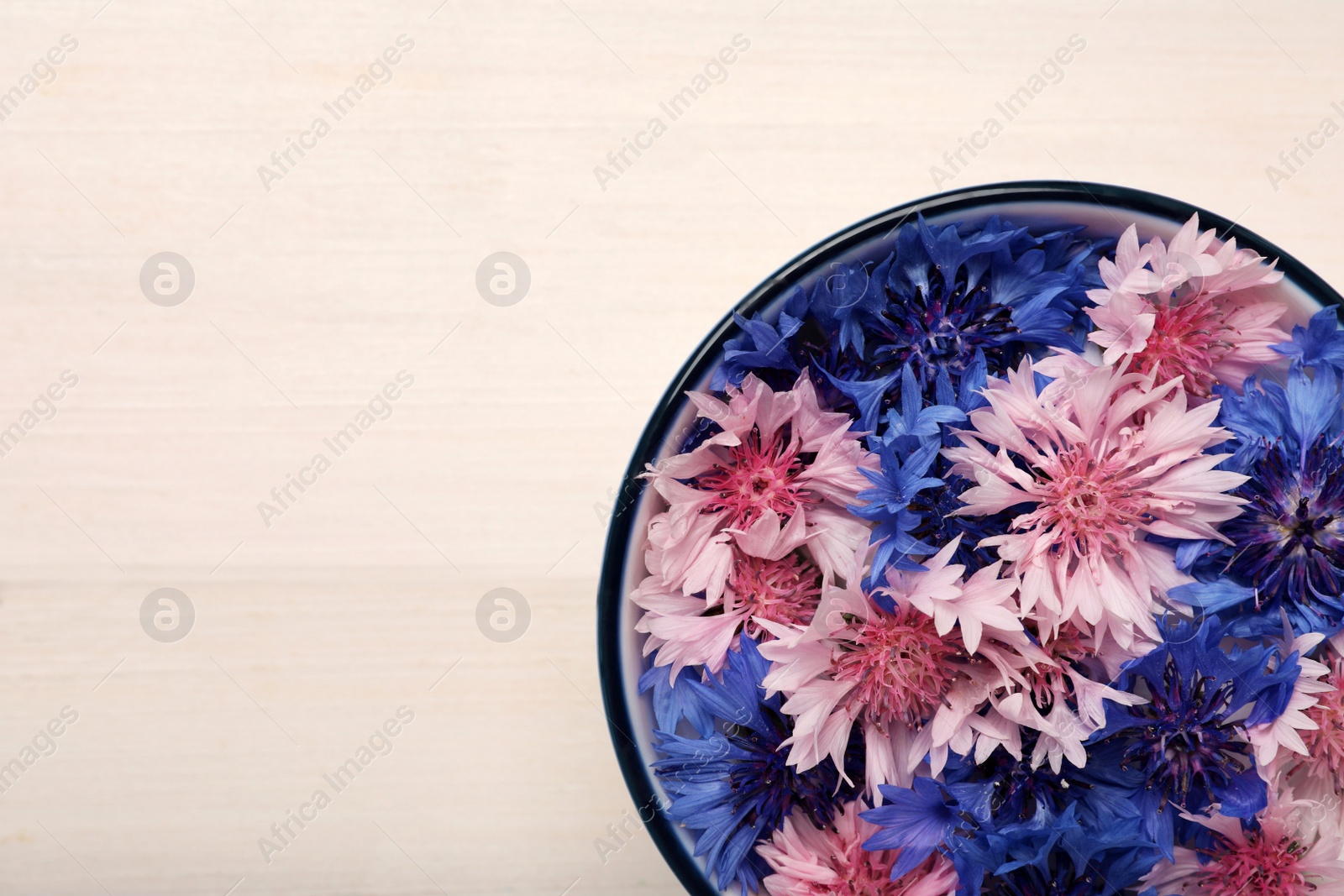 Photo of Beautiful colorful cornflowers in bowl on white wooden table, top view. Space for text