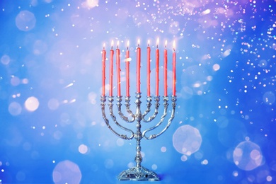 Image of Silver menorah with burning candles on light blue background, bokeh effect. Hanukkah celebration