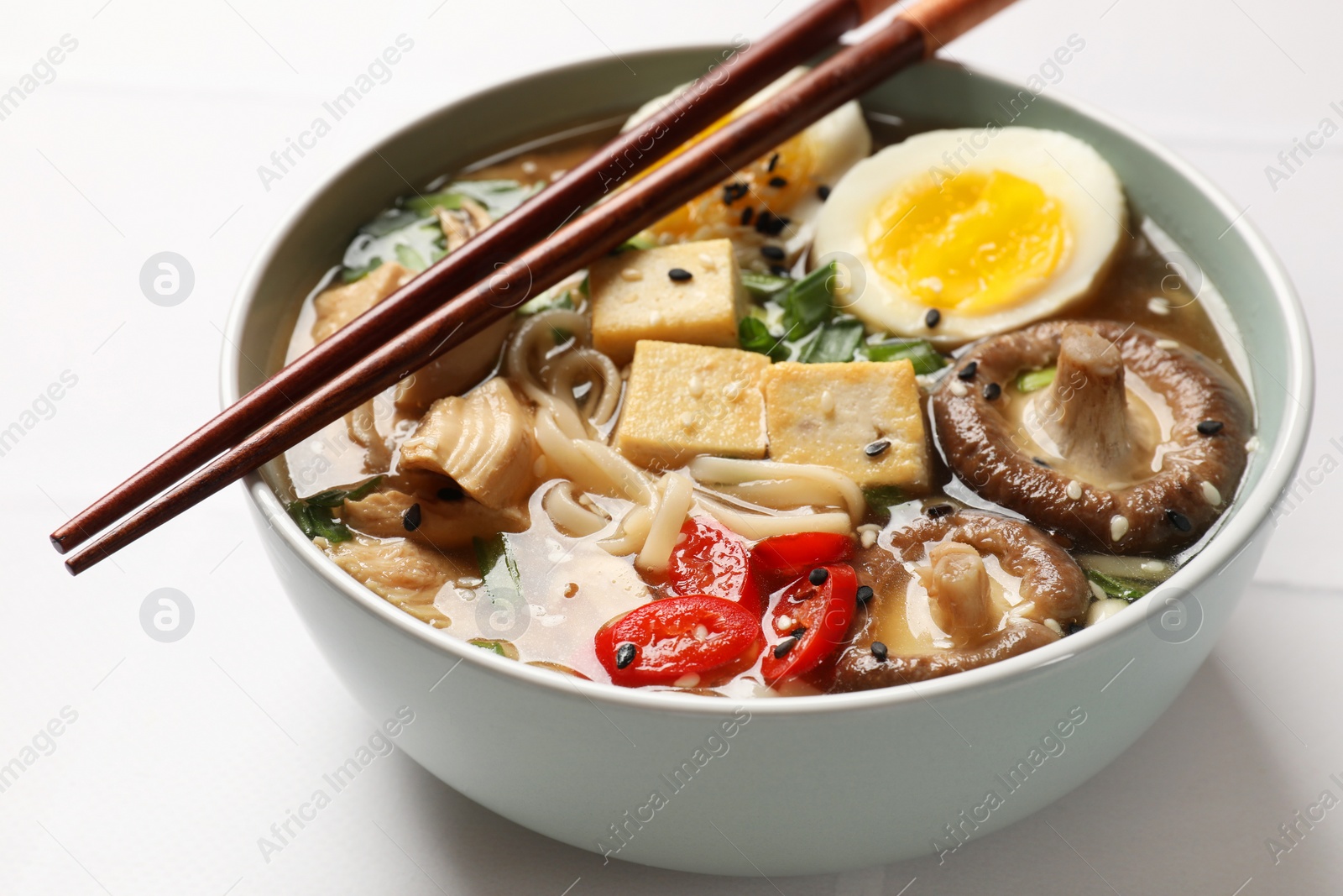 Photo of Noodle soup. Bowl of delicious ramen and chopsticks on white tiled table, closeup