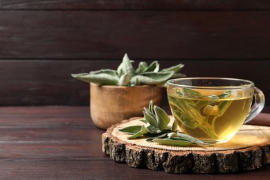 Cup of aromatic sage tea and fresh leaves on wooden table. Space for text