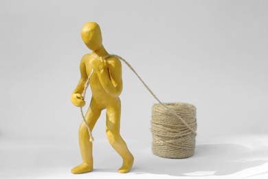 Photo of Human figure made of yellow plasticine carrying rope on white background