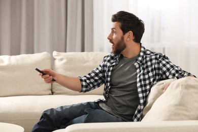 Photo of Surprised man watching TV on sofa at home