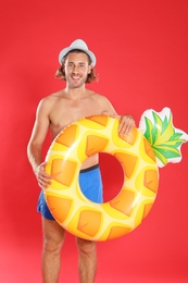 Attractive young man in beachwear with pineapple inflatable ring on red background