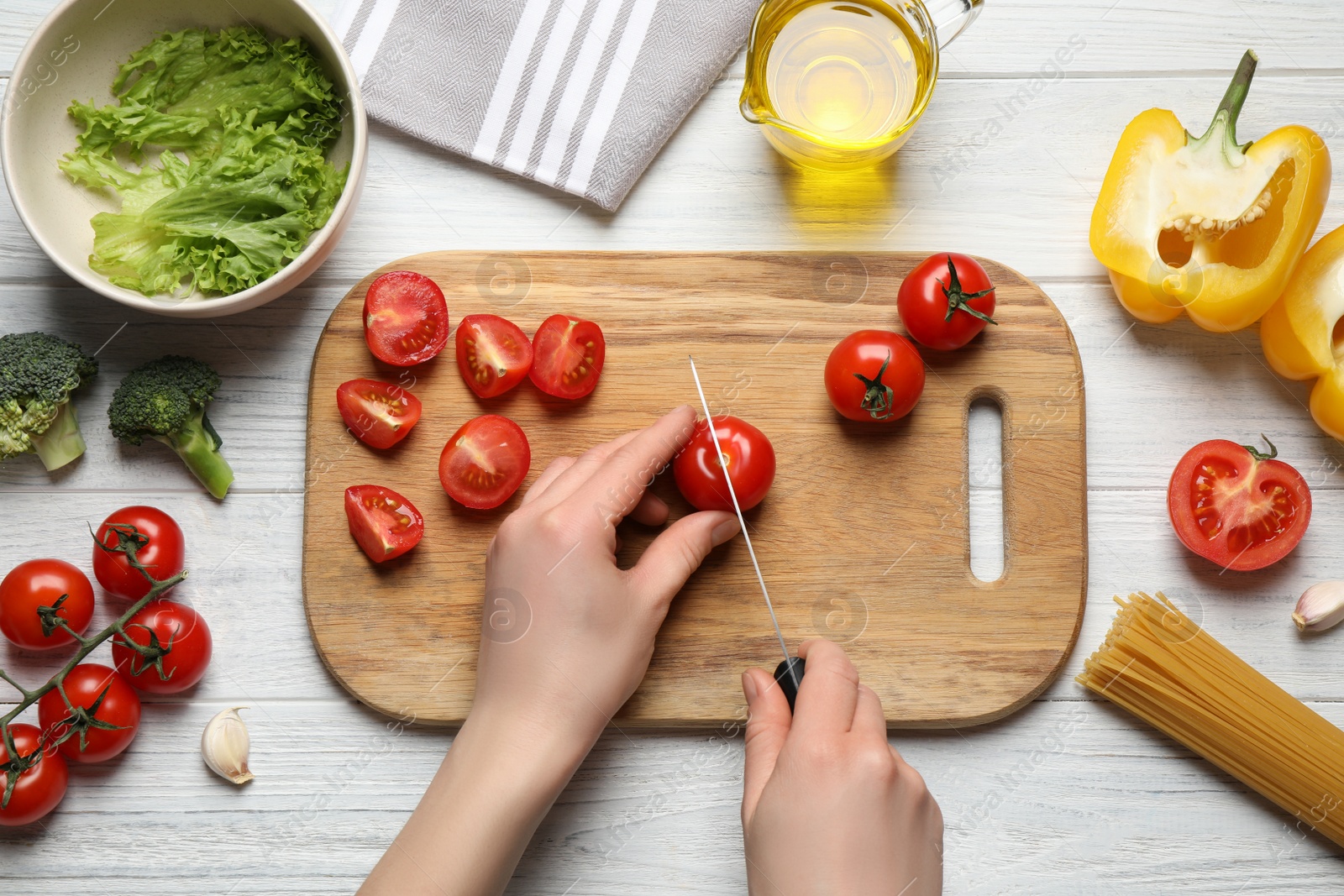 Photo of Woman cutting tomato at white wooden table, top view. Healthy cooking