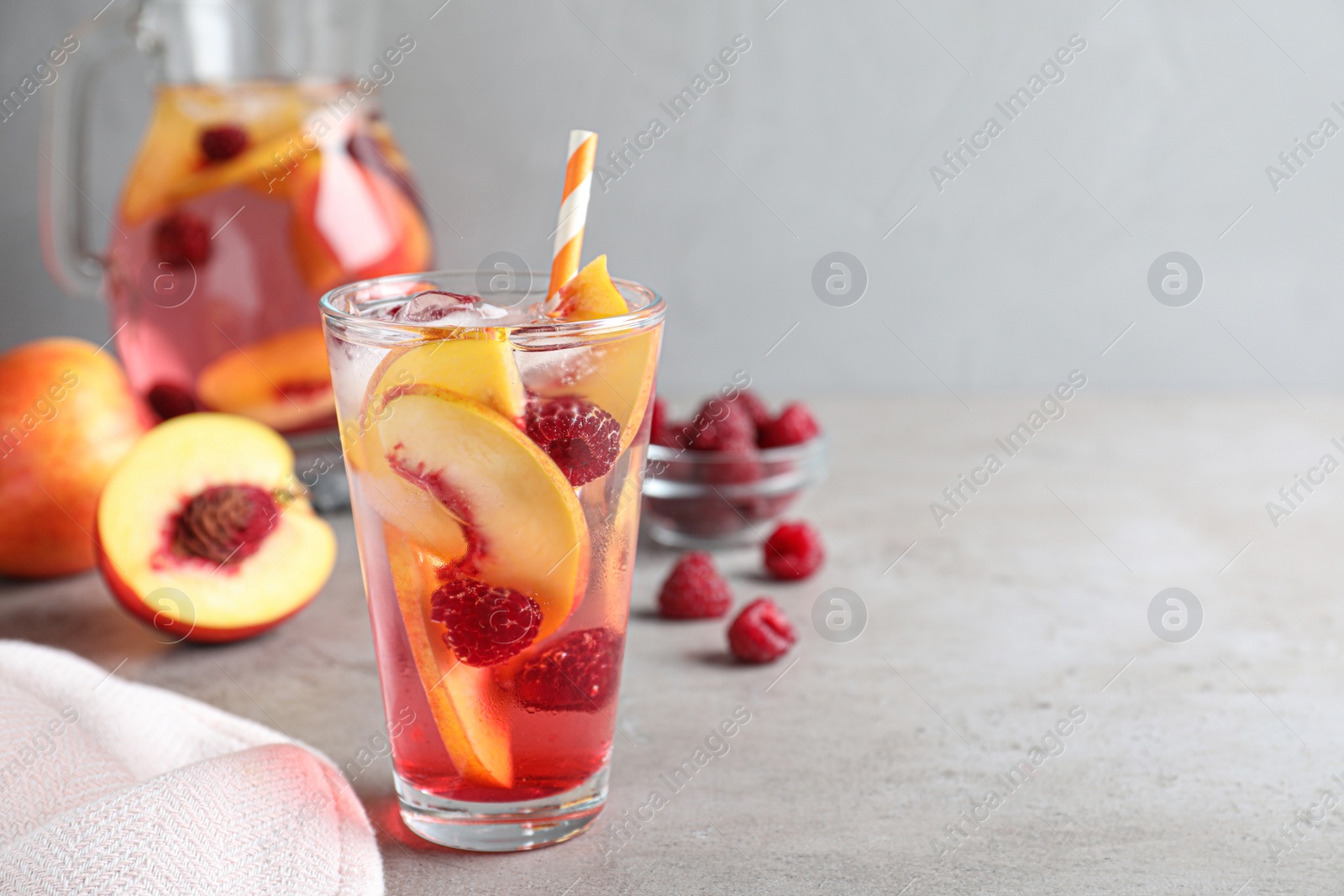 Photo of Delicious peach lemonade with soda water and raspberries on grey table, space for text. Fresh summer cocktail