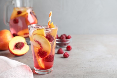 Delicious peach lemonade with soda water and raspberries on grey table, space for text. Fresh summer cocktail