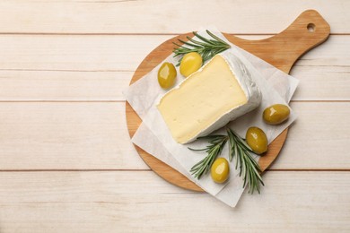 Board with piece of tasty camembert cheese, olives and rosemary on light wooden table, top view. Space for text