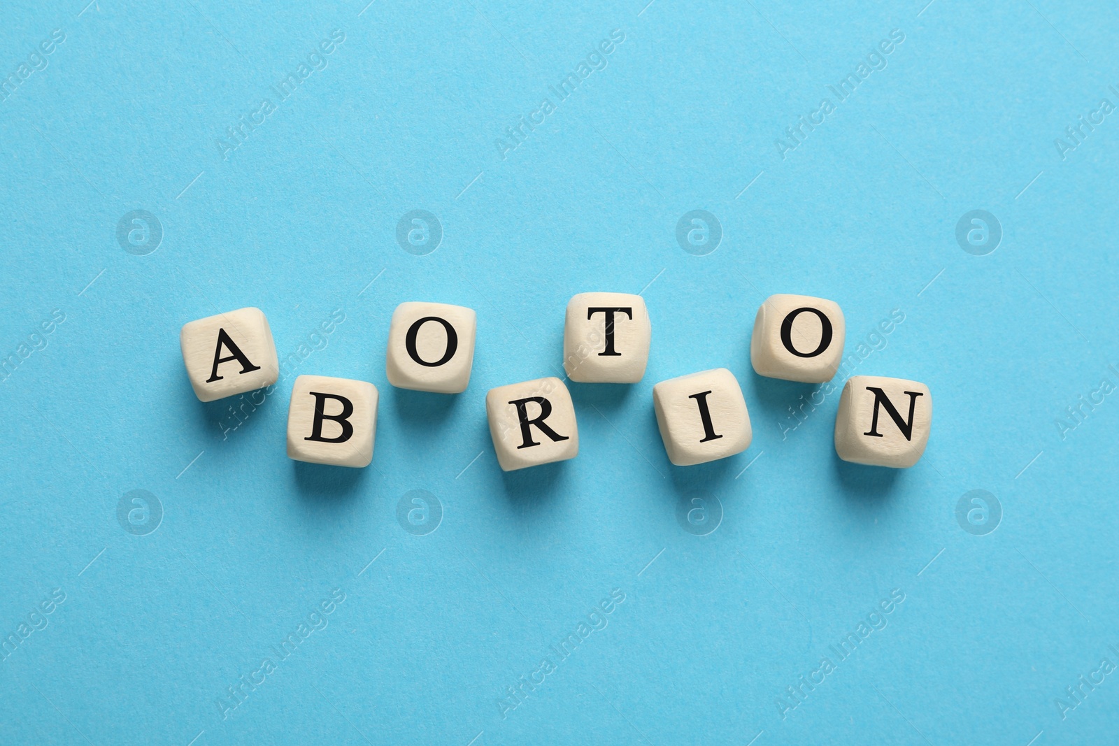 Photo of Word Abortion made of wooden cubes on light blue background, flat lay