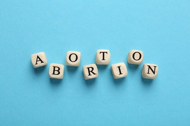Photo of Word Abortion made of wooden cubes on light blue background, flat lay