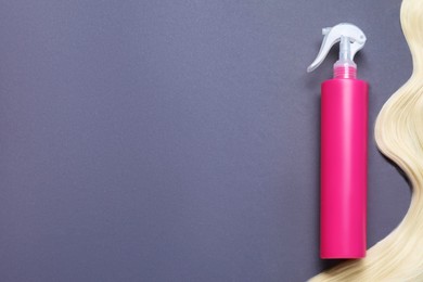 Photo of Spray bottle with thermal protection and lock of blonde hair on grey background, flat lay. Space for text