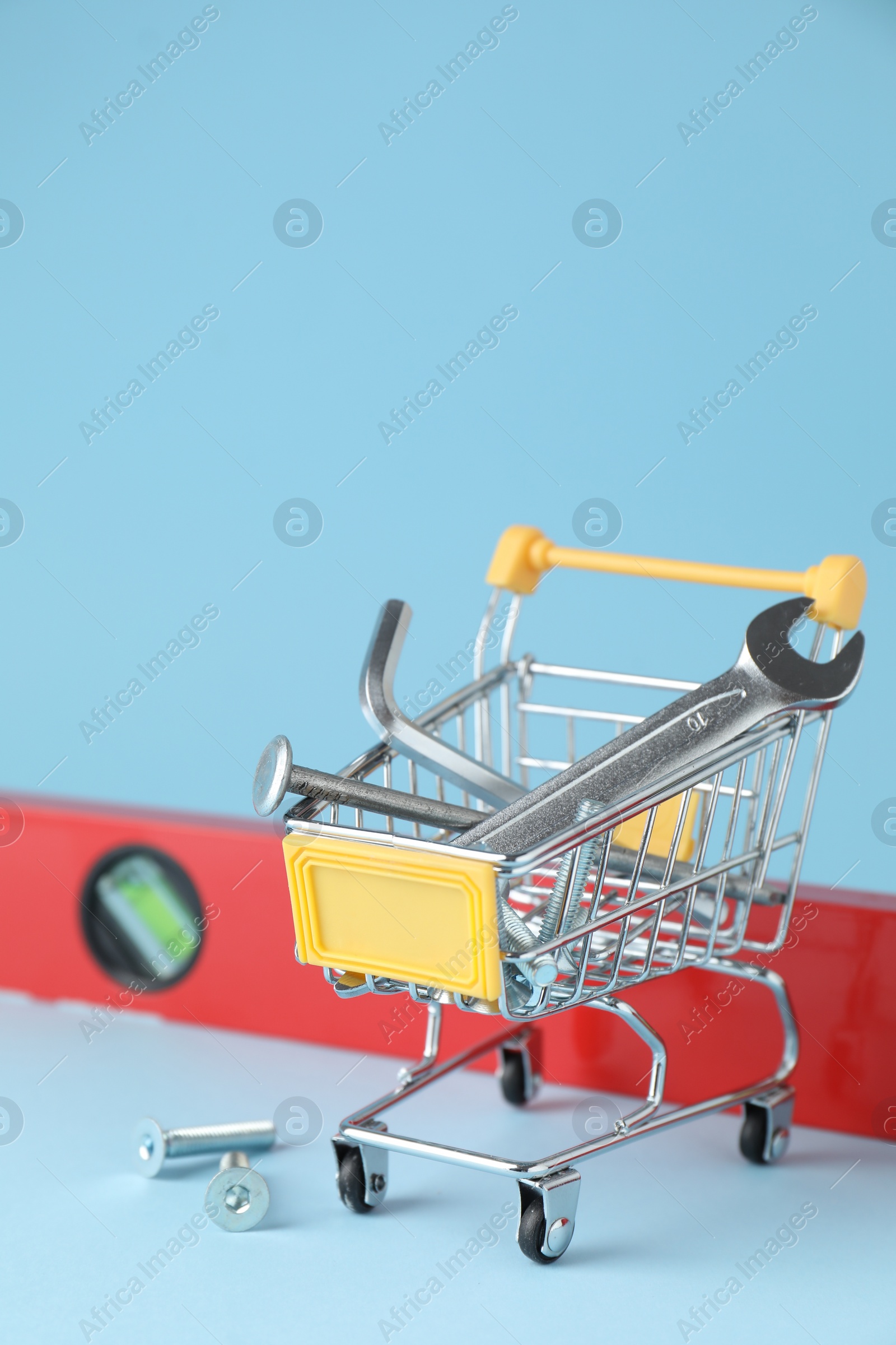 Photo of Shopping cart with different construction tools on light blue background, closeup