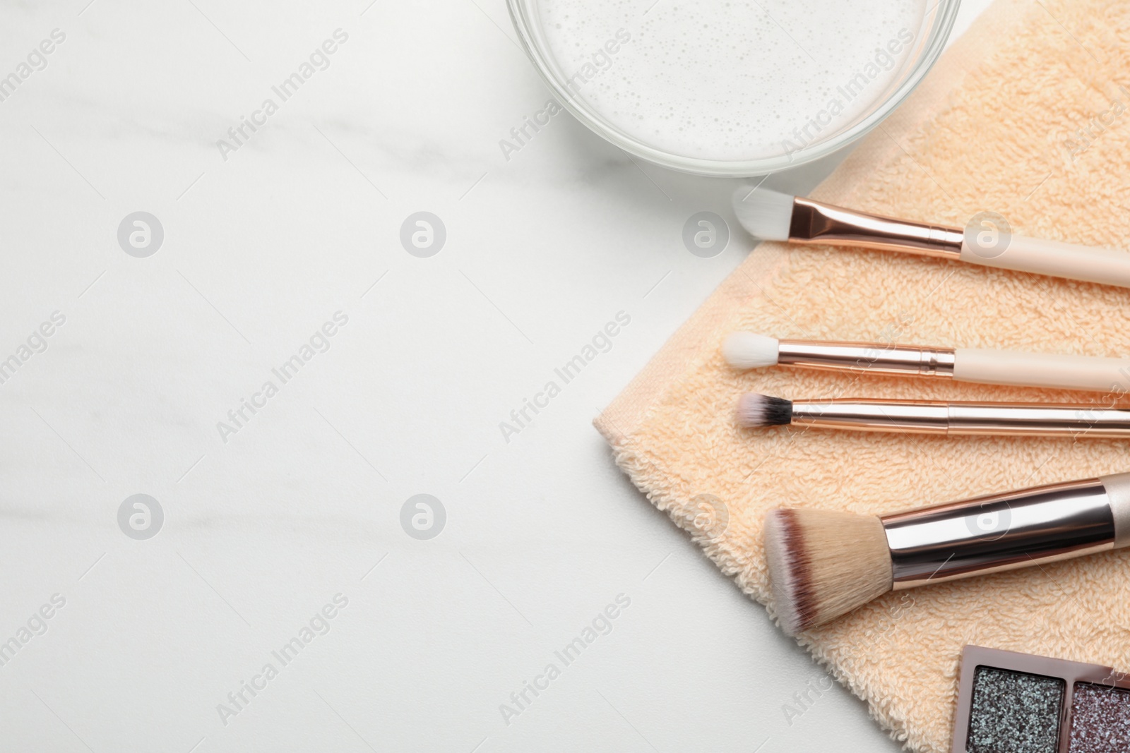 Photo of Clean makeup brushes with towel on white table, flat lay. Space for text