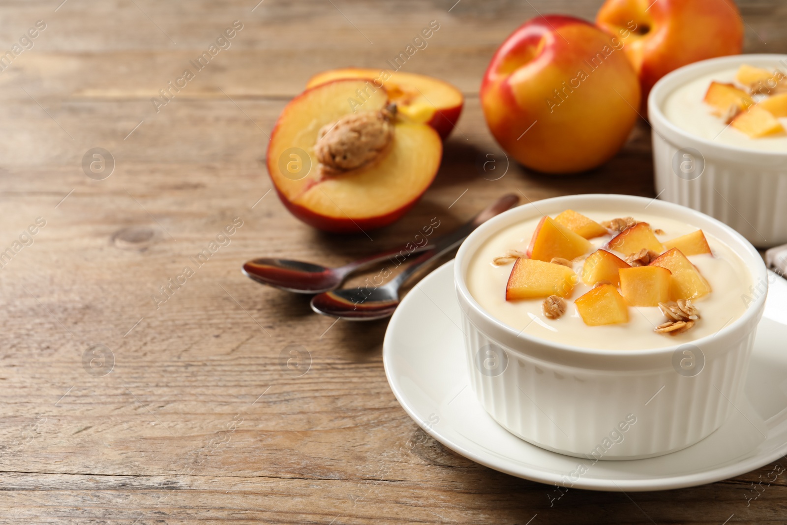 Photo of Tasty peach yogurt with granola and pieces of fruit in bowl on wooden table, space for text