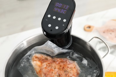 Photo of Sous vide cooker and vacuum packed meat in pot on white table, closeup. Thermal immersion circulator