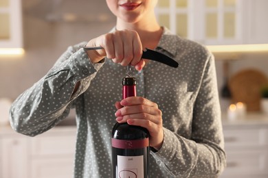Woman opening wine bottle with corkscrew in kitchen, closeup