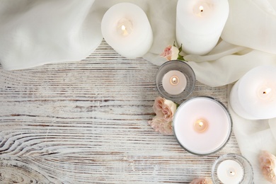 Photo of Flat lay composition with burning aromatic candles and roses on wooden table. Space for text