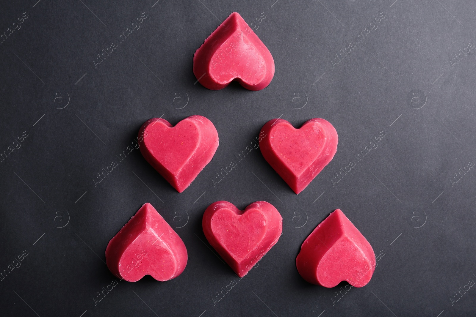 Photo of Heart shaped berry ice cubes on black background, flat lay