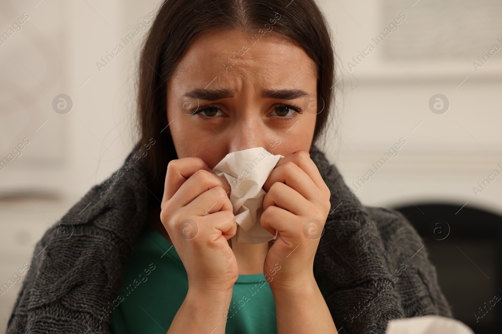 Photo of Sick woman wrapped in blanket with tissue blowing nose at home, closeup. Cold symptoms