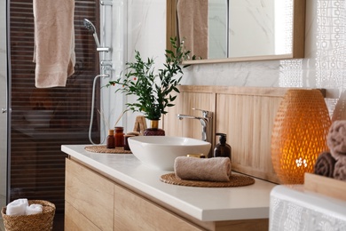 Photo of Vase with beautiful branches, candles and toiletries near vessel sink in bathroom. Interior design