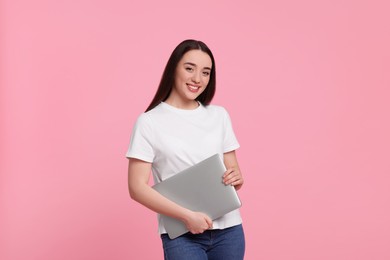 Smiling young woman with laptop on pink background