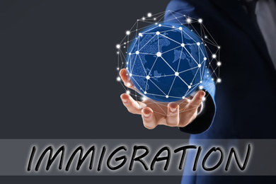 Image of Businessman holding world globe against dark grey background, closeup. Immigration concept