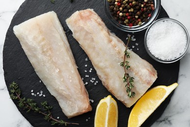 Photo of Fresh raw cod fillets, spices and lemon on white marble table, top view