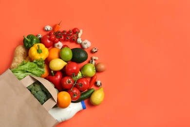 Photo of Paper bag with different groceries on coral background, flat lay. Space for text