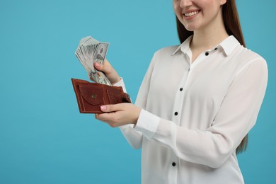 Photo of Woman putting money into wallet on light blue background, closeup