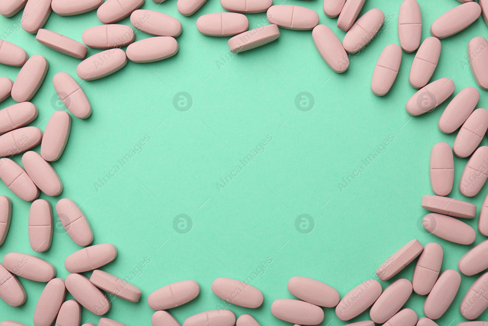 Photo of Frame made of pink vitamin capsules on turquoise background, top view. Space for text