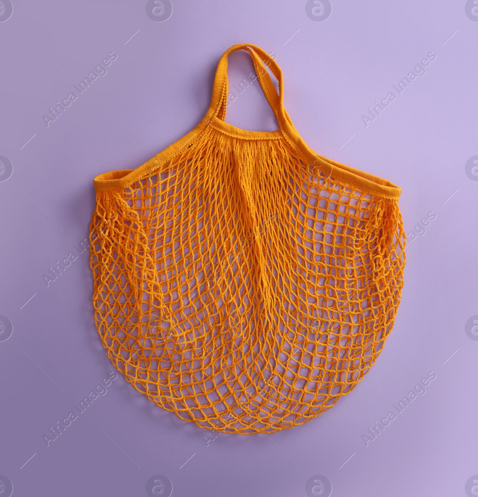 Photo of Empty orange net bag on lilac background, top view