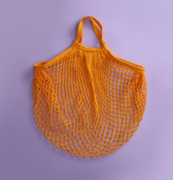 Empty orange net bag on lilac background, top view