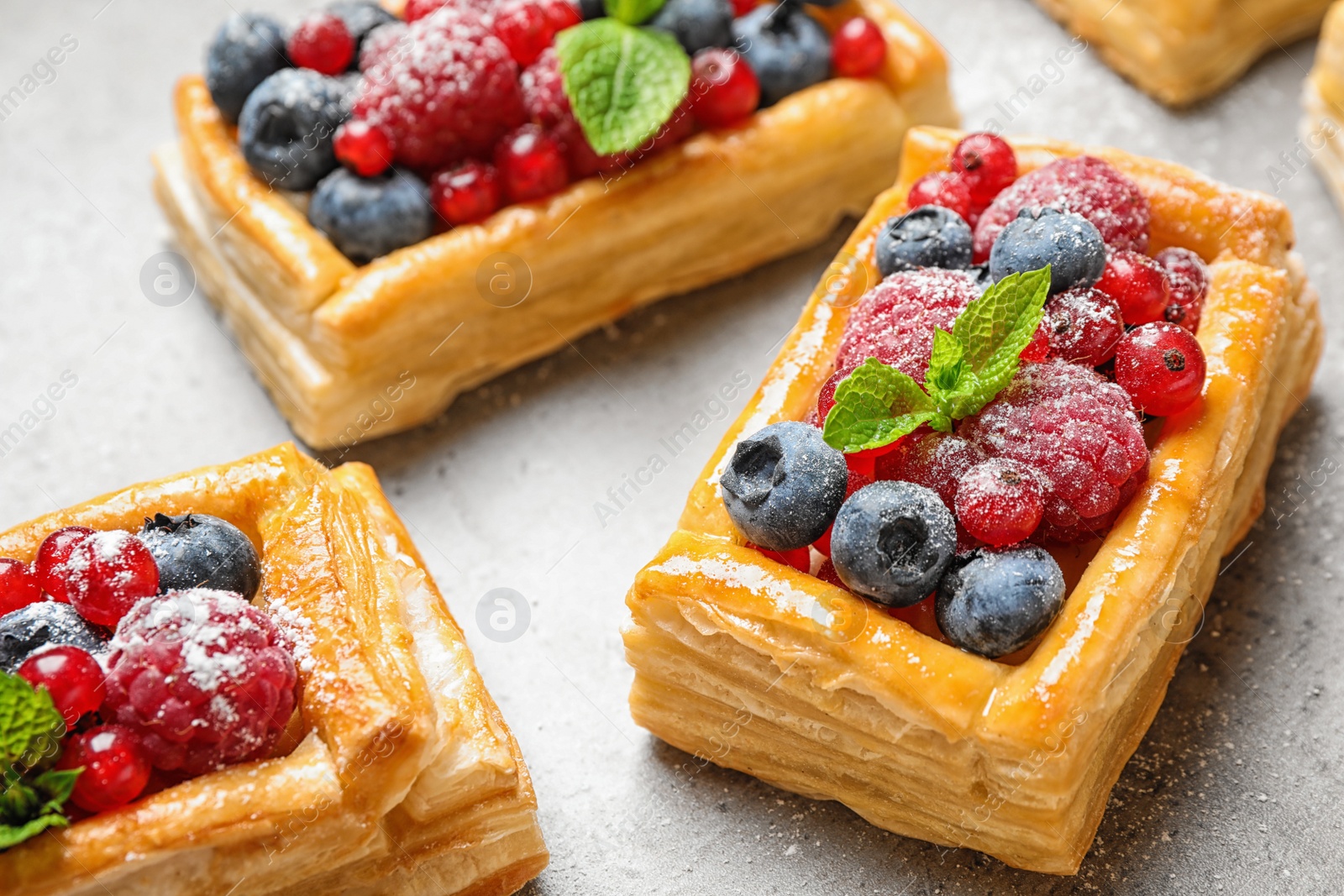 Photo of Fresh delicious puff pastry with sweet berries on grey table, closeup