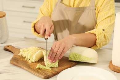 Photo of Woman cutting fresh chinese cabbage at table in kitchen, closeup