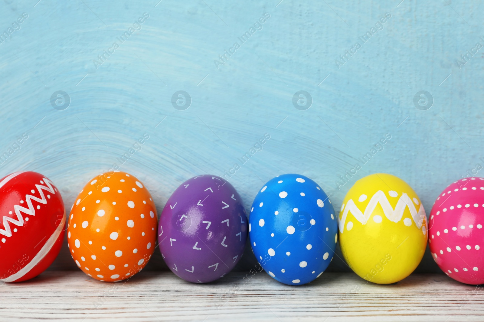 Photo of Decorated Easter eggs on table near color wall. Space for text